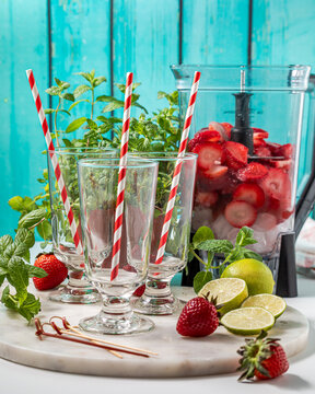 A blender with ingredients for making strawberry daiquiris with glasses in front