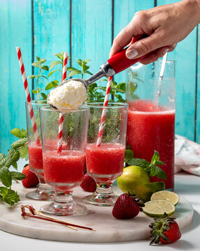 Glasses of freshly poured strawberry daiquiri with vanilla ice cream being added