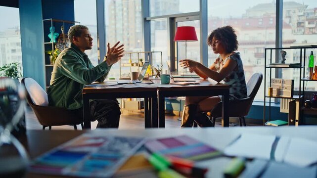Coworkers arguing across desk. Mixed race pair heated discussion modern office.