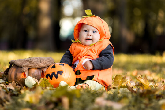 Cute baby in pumpkin costume sitting in autumn leaves with jack-o-lantern