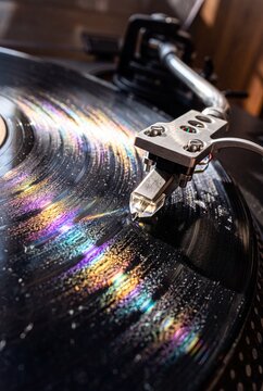 Close-up macro view of a vintage turntable needle playing a black vinyl record with rainbow prism light reflection on grooves
