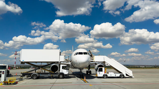 White passenger airplane on airport tarmac during ground handling. Commercial plane serviced by catering truck under blue sky with clouds. Aviation and travel concept