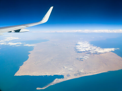 Aerial view from an airplane window showing the wing over a Port Bautino with vast desert coastline in Caspian sea, Kazakhstan. Commercial flight journey above an arid peninsula.