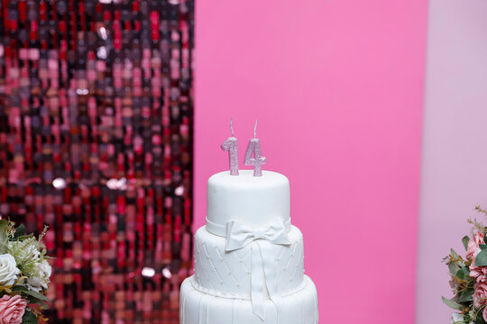 Elegant three tier white birthday cake with silver glitter fourteen candles in pink