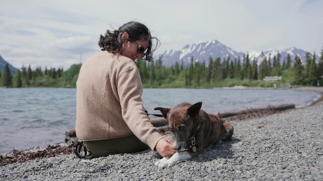 Woman playing with dog by a lake enjoying nature with mountains and forest in the background