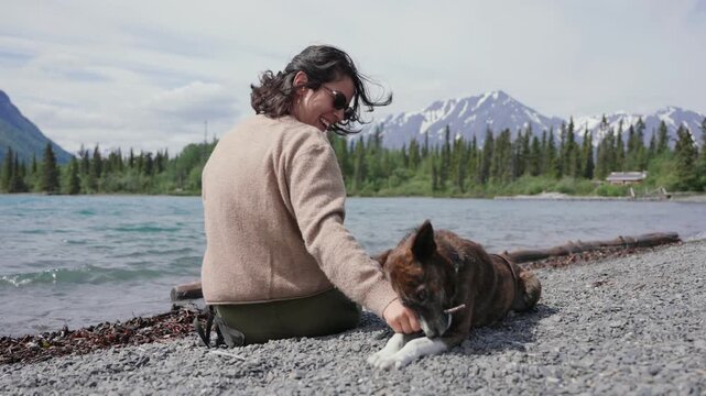 Woman playing with dog by a lake enjoying nature with mountains and forest in the background