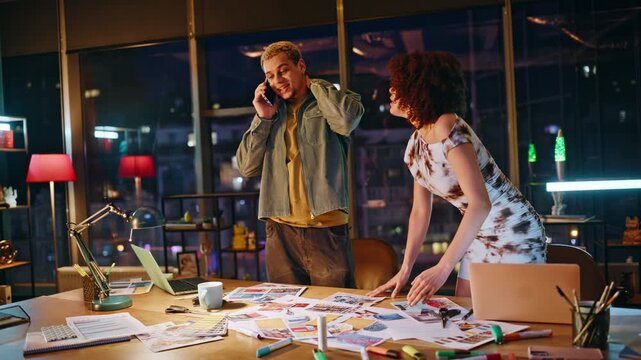 Coworkers celebrating good news on phone call in design office at night teamwork