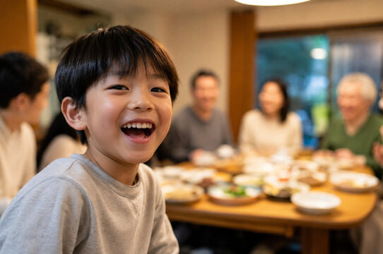 Joyful Asian child laughing in crisp foreground focus during a warm family dinner, while relatives and shared dishes blur softly in the background.
