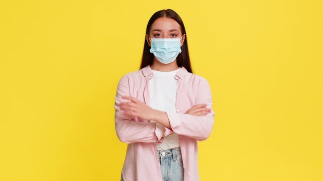 Young woman carefully putting on medical mask, showing preventive behavior protection caution against illness. Girl on yellow background demonstrates responsibility, awareness and personal health care