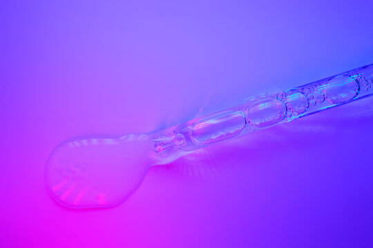 Dropping cosmetic serum with a pipette on neon background