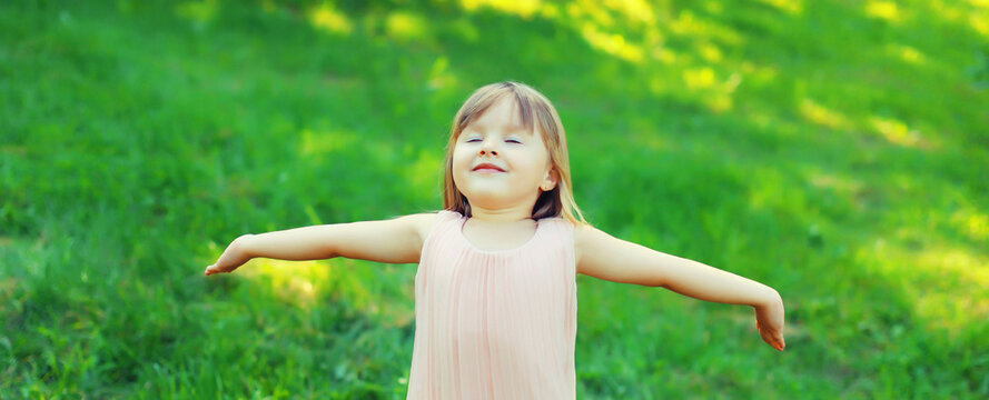 Happy little girl child enjoying warm weather standing on the grass in summer green park