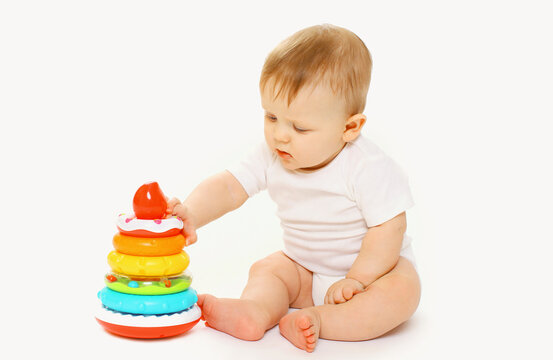 Happy little baby playing with toys sitting on floor on white studio background