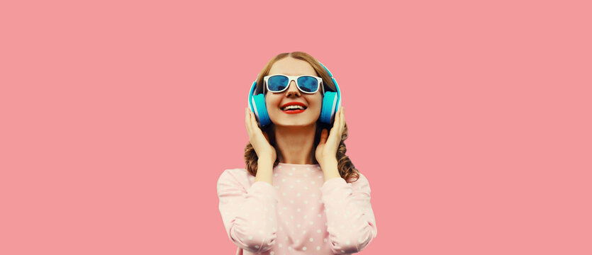 Portrait of happy smiling young woman listening to music in wireless headphones on pink background