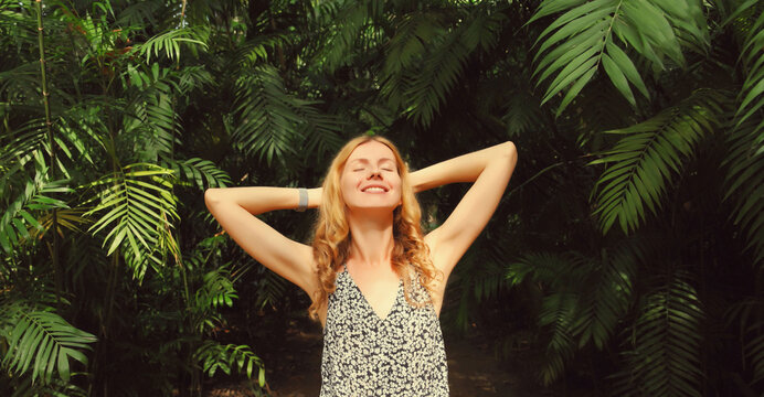Happy smiling young woman enjoying nature in forest on tropical tree background