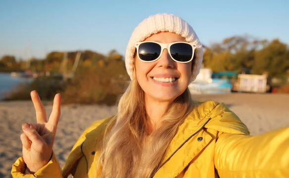 Happy smiling woman taking selfie with smartphone on beach, joyful female using phone on sea coast