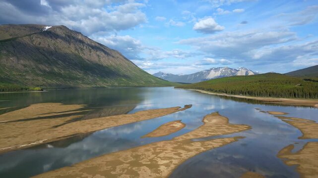 Drone aerial view of Grayling Bay beach, lake, and mountains creating patterns with cloud reflections in Yukon, Canada
