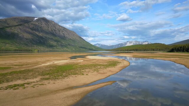 Drone aerial view of Grayling Bay beach, lake, and mountains creating patterns with cloud reflections in Yukon, Canada
