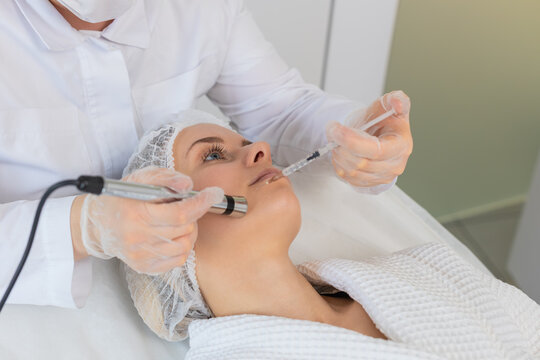 Injection-free mesotherapy or electroporation. Beautician doctor makes client middle-aged woman face therapy in beauty clinic salon. Girl skin care anti-age spa procedure. Aesthetic cosmetology.