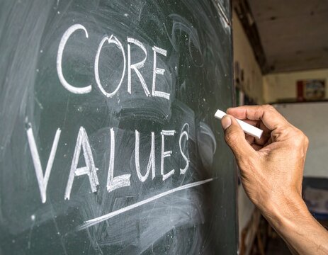 A hand draws the words core values on a blackboard, demonstrating the importance of ethical principles in business and personal life today and beyond.