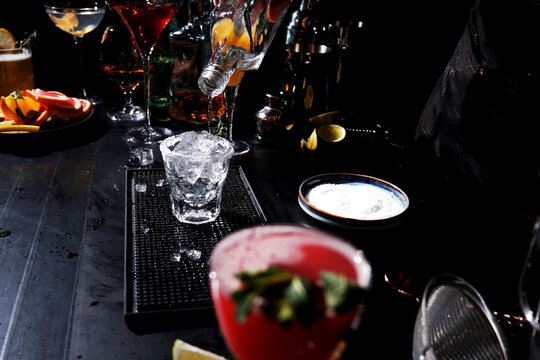 Professional over bar counter pouring clear liquor into iced glass. Mixing process of strong craft beverage.