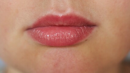 Obraz premium Close-up of a woman's full lips with glossy pink lipstick and subtle freckles