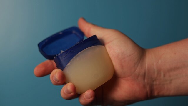 Hand holding an open jar of petroleum jelly for skin care