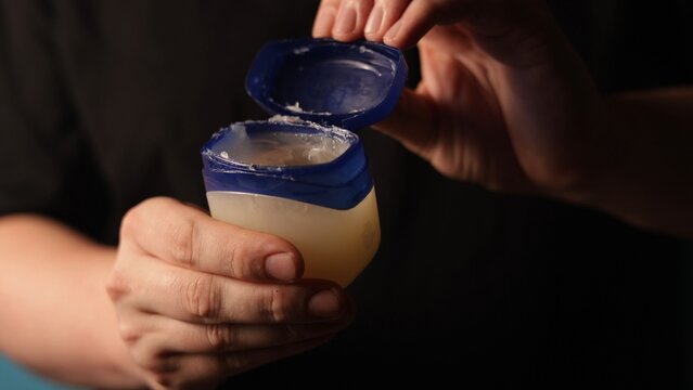 Hands opening a small jar of petroleum jelly for skin care