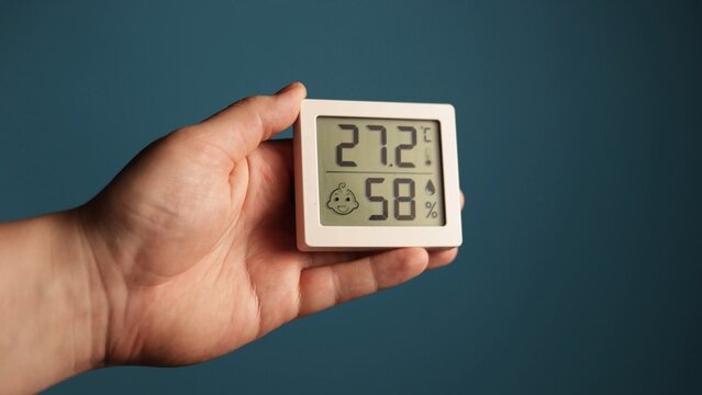 Digital thermometer and hygrometer held in hand showing temperature and humidity