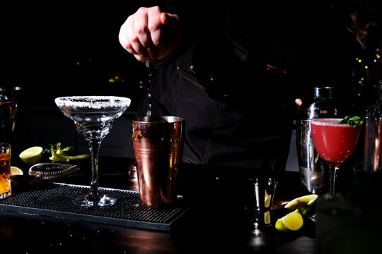 Margarita tequila cocktail preparation in bartender hand at dark bar counter. Fresh sour citrus alcoholic beverage concept.