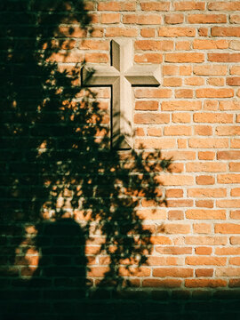 Stone Christian cross on red brick wall, religious symbol with tree shadow, sacred church architecture exterior, spiritual faith concept
