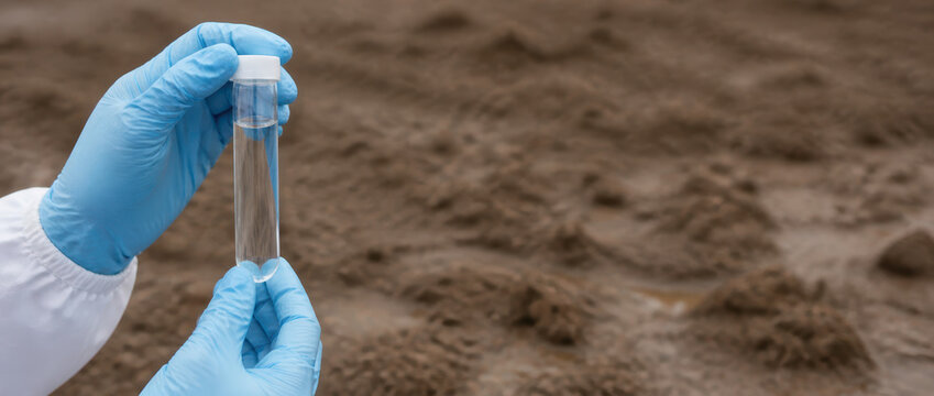 Water scarcity climate adaptation test with gloved hand holding sample vial over dry soil