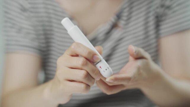 Close up of a woman holding a lancing device before fingertip blood testing for glucose monitoring, representing diabetes management, home medical care, self testing, disease prevention, and healthy l
