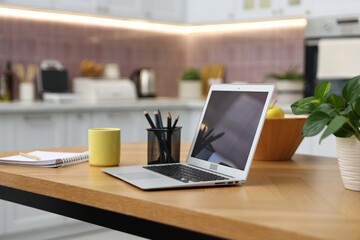 Obraz na płótnie Canvas Workplace with laptop, mug, stationery, houseplant and fruits on wooden table indoors, closeup