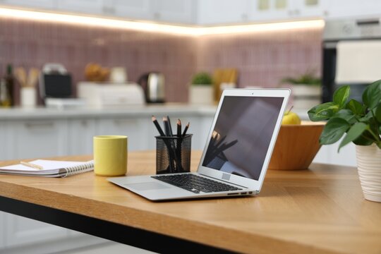 Workplace with laptop, mug, stationery, houseplant and fruits on wooden table indoors, closeup