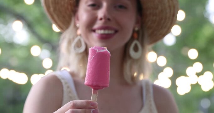 Happy woman in hat eating delicious ice pop in park. Camera moving backwards
