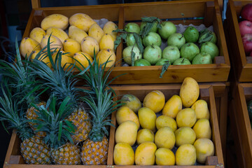 Fresh tropical fruits displayed in wooden crates at local market stall. Ripe mangoes pineapples and guavas arranged at Vietnamese fruit market © Aisylu