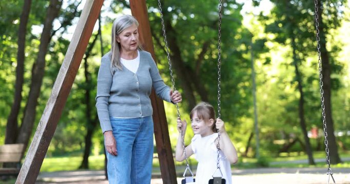 Grandmother pushing her granddaughter on swing in park