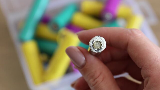 Woman with used alkaline battery at table, closeup. Waste recycling