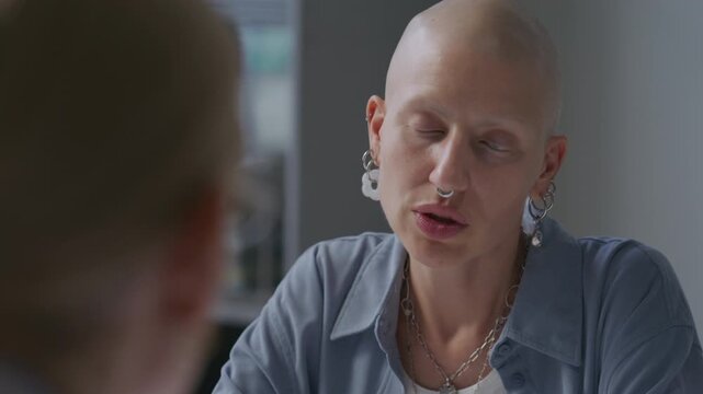 Female cancer patient with bald head listening attentively to doctor and nodding during medical consultation at clinic