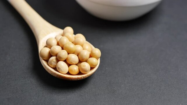 Close-up shot of dry soybeans on wooden spoon, rotating slowly on black background, showcasing detail and texture for culinary and agricultural themes
