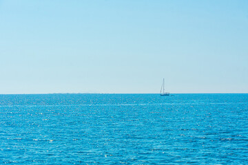 Obraz premium Minimal seascape with a single white sailboat on the horizon across a calm open blue sea, freedom, summer sailing, coastal escape, Turkey.