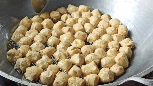 Fresh tofu being fried in hot oil during the preparation of crispy tahu kremes, showcasing the cooking process, golden texture, and traditional Indonesian culinary craftsmanship.