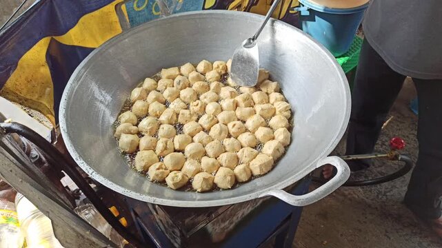 Fresh tofu being fried in hot oil during the preparation of crispy tahu kremes, showcasing the cooking process, golden texture, and traditional Indonesian culinary craftsmanship.