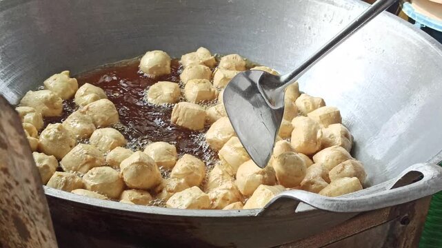 Fresh tofu being fried in hot oil during the preparation of crispy tahu kremes, showcasing the cooking process, golden texture, and traditional Indonesian culinary craftsmanship.