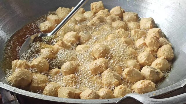 Fresh tofu being fried in hot oil during the preparation of crispy tahu kremes, showcasing the cooking process, golden texture, and traditional Indonesian culinary craftsmanship.