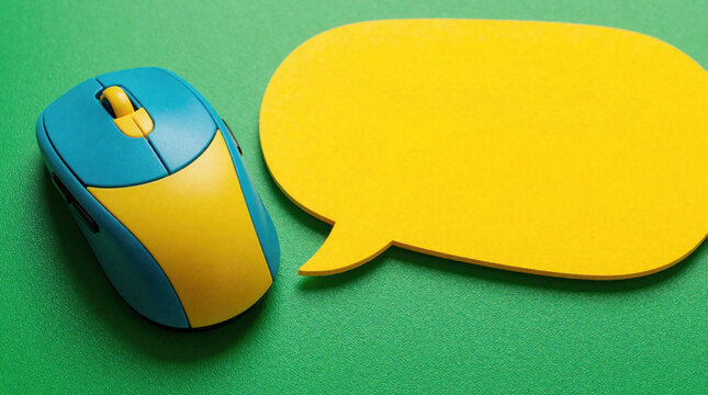 Blue and yellow computer mouse rests on a green surface near a large yellow speech bubble. The bubble contains text that reads QA. This symbolizes digital communication and interaction.