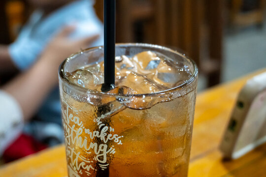 Close up of a glass of iced tea with condensation and a black straw