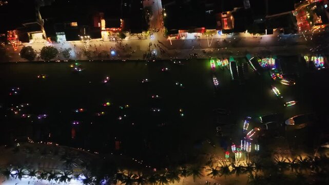Colorful lanterns light up boats on the water in Hoi An, Vietnam, with people walking along the riverside enjoying the vibrant night scene