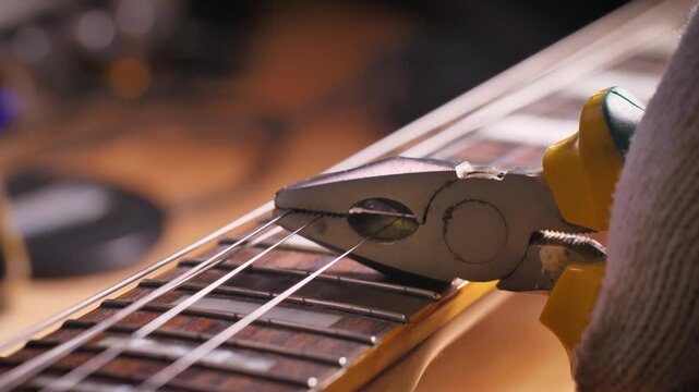Close up footage of pliers cutting a guitar string on an electric guitar fretboard during maintenance and restringing. Shallow depth of field with warm workshop lighting