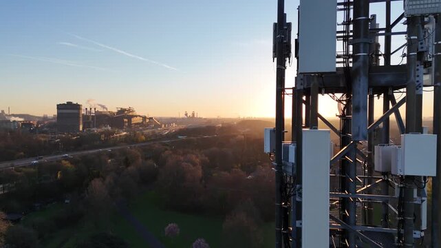 Drone climbs beside the mast toward the antennas, revealing industrial grounds and motorway from an upward moving close angle.